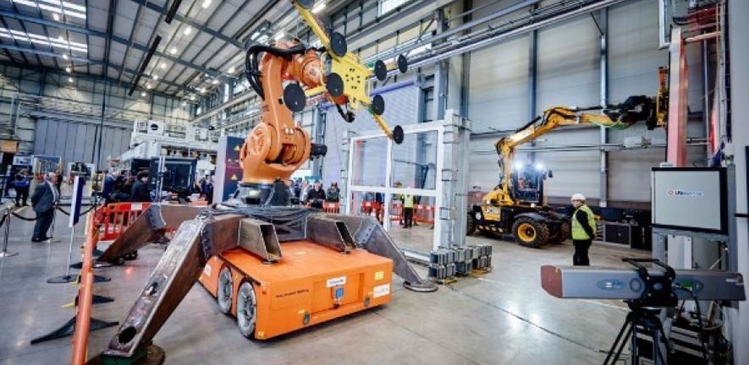 Avansert industriell robotarm på mobil plattform i et anlegg, utstyrt for glasshåndtering, demonstrerer automasjon i byggeprosesser. Fagfolk observerer i bakgrunnen.